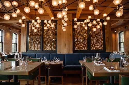 A stylish restaurant interior featuring wooden beams, decorative lighting, and elegant table settings.