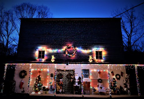 A festive house adorned with colorful Christmas lights, wreaths, and decorations, set against a twilight sky.