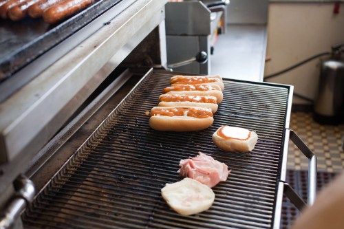 Grilled hot dogs on a rack with buns and slices of meat nearby in a kitchen setting.
