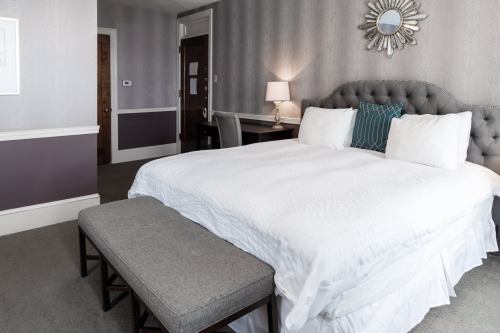 A cozy hotel room featuring a large bed, decorative mirror, and a bench at the foot of the bed.