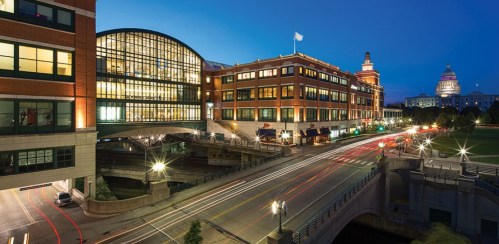 Cityscape at dusk featuring modern buildings, a busy street, and a historic dome in the background.