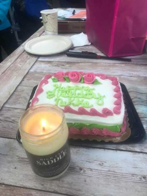 A decorated cake with pink roses and green accents next to a lit candle on a wooden table.