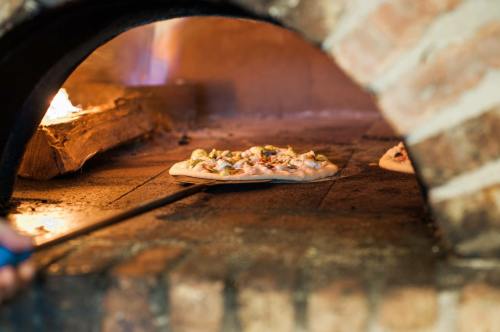 A pizza being placed in a brick oven with flames visible in the background.