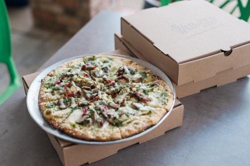 A freshly baked pizza topped with mushrooms, herbs, and sun-dried tomatoes, placed on a table next to two pizza boxes.