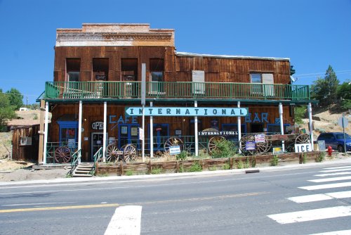 Historic wooden building with "International Cafe" sign, featuring a balcony and old wagons outside, set along a road.