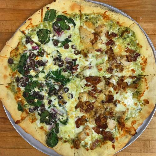 A pizza divided into four sections, topped with spinach, olives, chicken, and a creamy sauce on a golden crust.