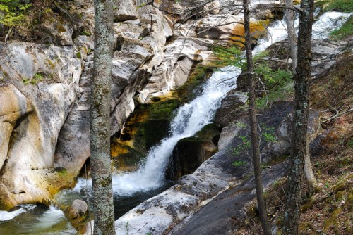 A serene waterfall cascades over rocky terrain, surrounded by trees and lush greenery.