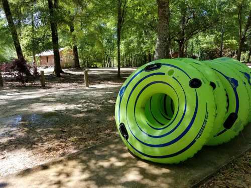 A stack of bright green and blue inflatable tubes sits on a path in a wooded area with a cabin in the background.