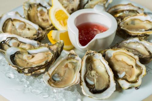 A plate of fresh oysters on ice, garnished with lemon wedges and a small bowl of cocktail sauce.