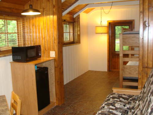 Cozy cabin interior featuring a kitchenette, bunk beds, and wooden walls, with natural light from windows.