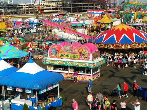 A vibrant fairground scene with colorful tents, food stalls, and people enjoying rides and attractions.