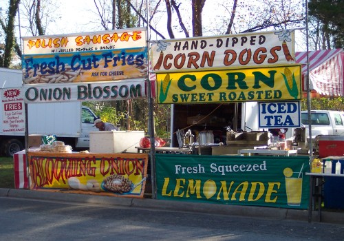 Colorful food stall featuring signs for Polish sausage, corn dogs, fresh fries, onion blossoms, and lemonade.