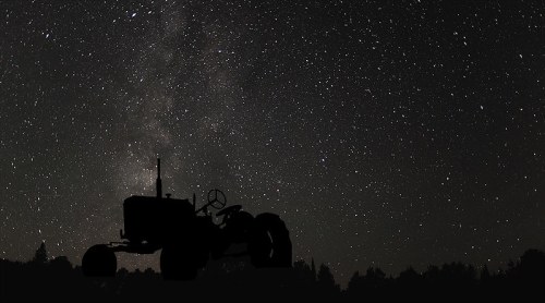 Silhouette of a tractor against a starry night sky with the Milky Way visible.