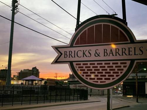 Sign for "Bricks & Barrels" with a sunset in the background, featuring buildings and power lines.