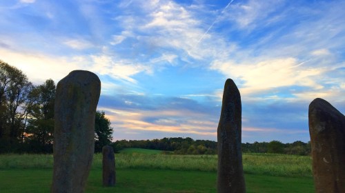 A serene landscape featuring tall stone monoliths against a colorful sky and lush green fields.