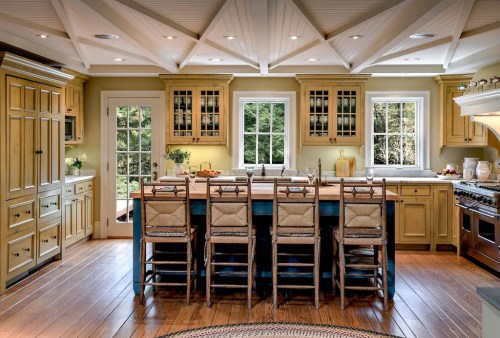 A spacious kitchen with yellow cabinetry, a large island with seating, and large windows overlooking greenery.