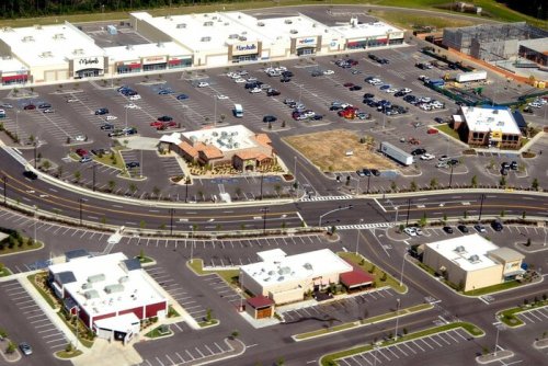 Aerial view of a shopping center with multiple stores, a large parking lot, and surrounding roads.