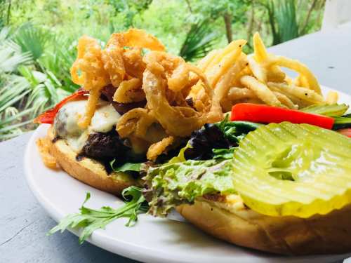 A close-up of a burger with lettuce, pickles, and crispy onion rings, served with fries on a white plate.