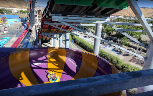 A colorful water slide with a view from above, showing a rider in a raft entering a large, swirling bowl.