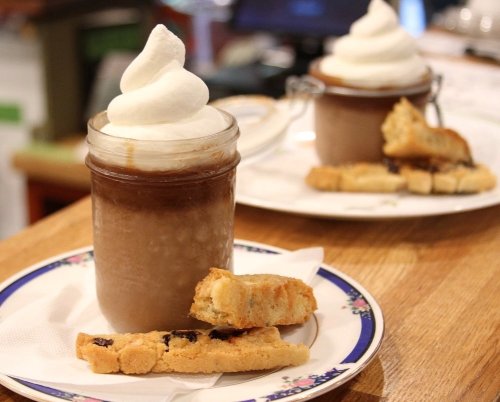 A glass jar filled with chocolate drink topped with whipped cream, accompanied by biscotti on a plate.