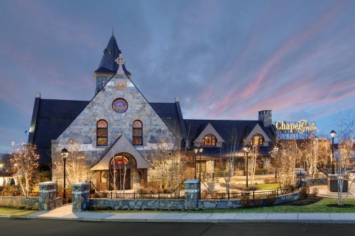 A stone building with a steeple, illuminated by lights, set against a colorful sunset sky. "Chapel" sign visible.