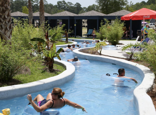 People float on inner tubes in a winding lazy river surrounded by lush greenery and shaded cabanas.
