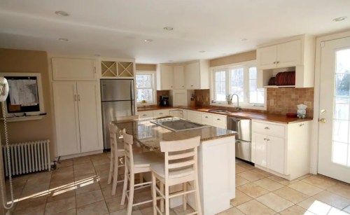 Bright kitchen with white cabinets, a central island, stainless steel appliances, and large windows for natural light.