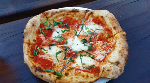 A freshly baked pizza topped with tomato sauce, mozzarella cheese, and fresh basil on a wooden table.