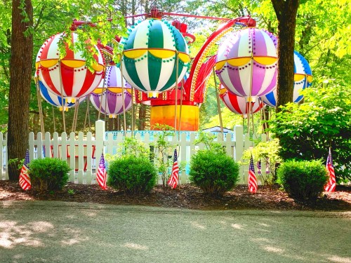 Colorful hot air balloon decorations in a park, surrounded by greenery and small American flags along a pathway.