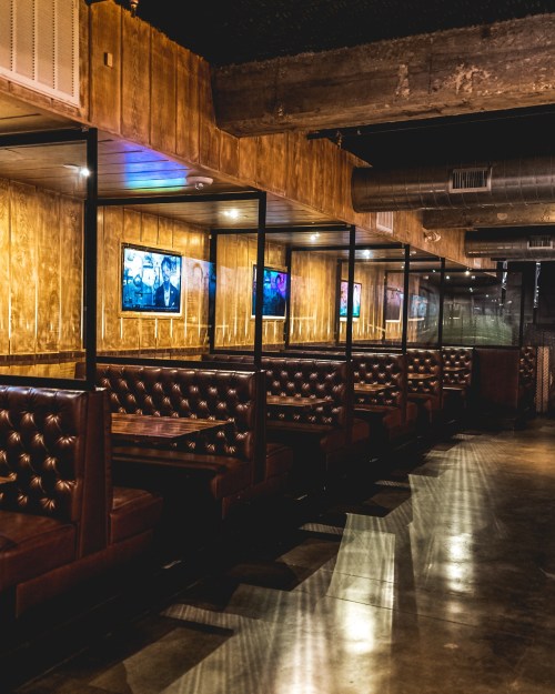 A modern restaurant interior featuring leather booths, wooden walls, and framed artwork on display.