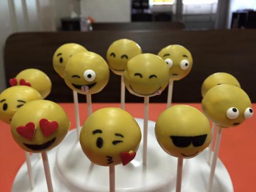 A display of yellow emoji cake pops with various facial expressions on a white stand.