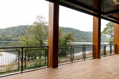 View from a wooden deck overlooking a calm river and green hills on a cloudy day.