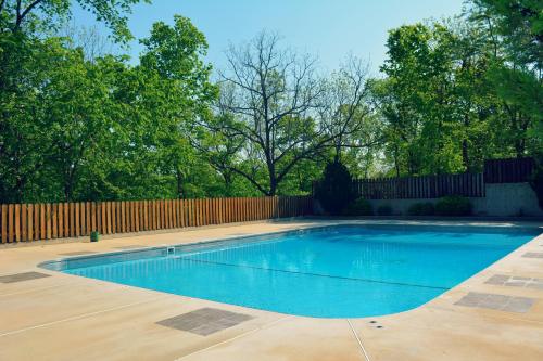 A clear blue swimming pool surrounded by trees and a wooden fence on a sunny day.