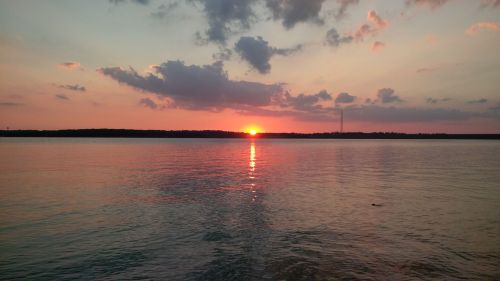 A serene sunset over calm waters, with vibrant colors reflecting on the surface and clouds scattered in the sky.