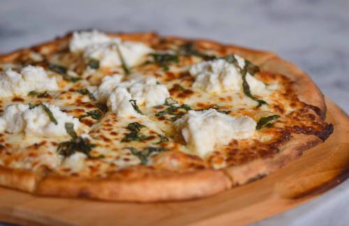 A freshly baked pizza topped with dollops of ricotta cheese and fresh basil on a wooden serving board.