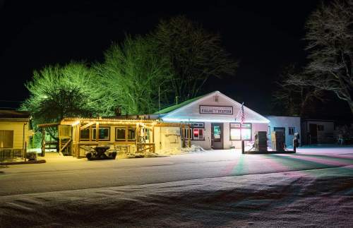 A brightly lit building at night, surrounded by trees, with colorful lights illuminating the snowy ground.