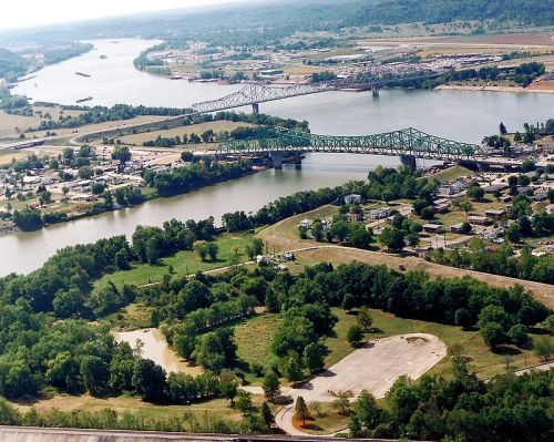 Aerial view of a river with bridges, green landscapes, and a small town in the background.