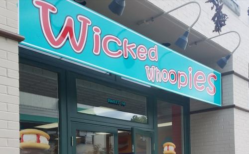 Sign for "Wicked Whoopies" shop with colorful lettering above the entrance, featuring a dessert illustration.