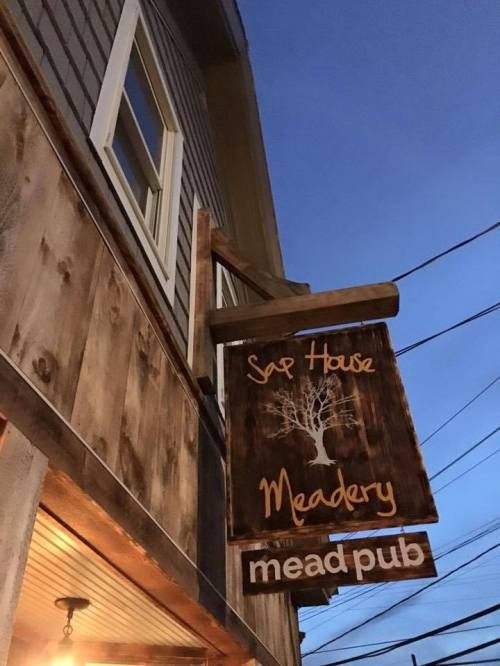 Sign for Sap House Meadery, a mead pub, hanging from a wooden building against a twilight sky.