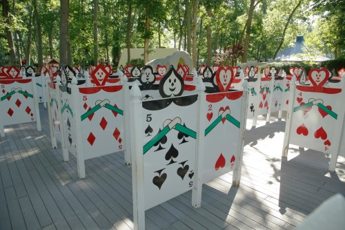A whimsical outdoor installation featuring large playing card-themed structures in a wooded area.