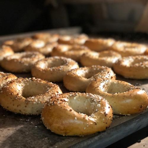 A tray of freshly baked bagels sprinkled with seeds, arranged in a warm, inviting display.