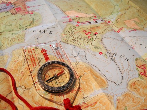 A compass rests on a detailed topographic map, highlighting terrain features and trails.