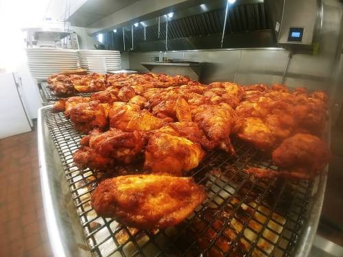 A large tray of golden-brown, crispy chicken wings cooling on a rack in a commercial kitchen.