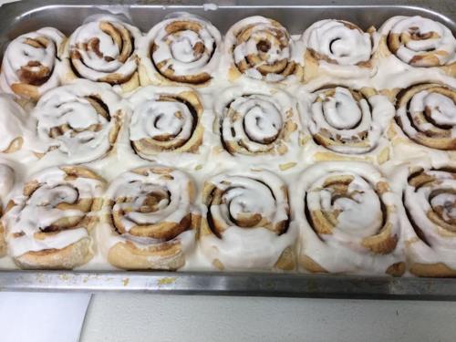 A tray of freshly baked cinnamon rolls topped with creamy icing, arranged in neat rows.