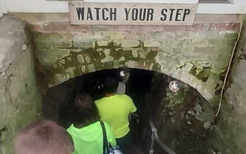 A group of people descends a dimly lit staircase with a "Watch Your Step" sign above.