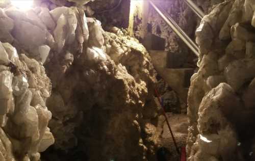 A dimly lit cave with large crystal formations and a staircase leading up, creating a natural, rocky environment.