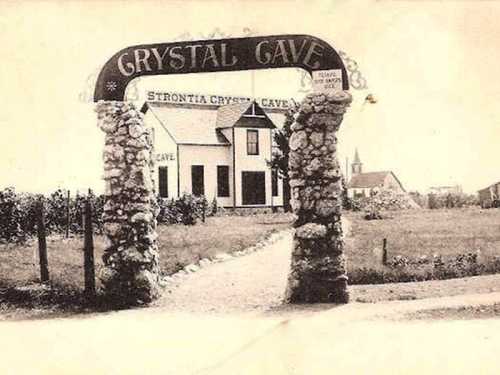 Historic entrance to Crystal Cave, featuring a stone archway and a building in the background, surrounded by fields.