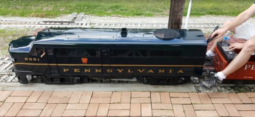 A model train labeled "PENNSYLVANIA" on a track, with a person sitting beside it.