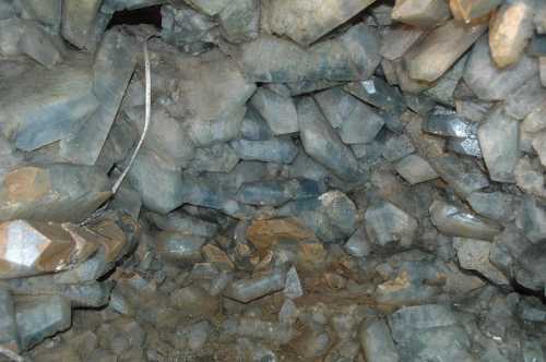 A close-up view of a cave interior filled with large, irregularly shaped blue-gray crystals and rocky surfaces.