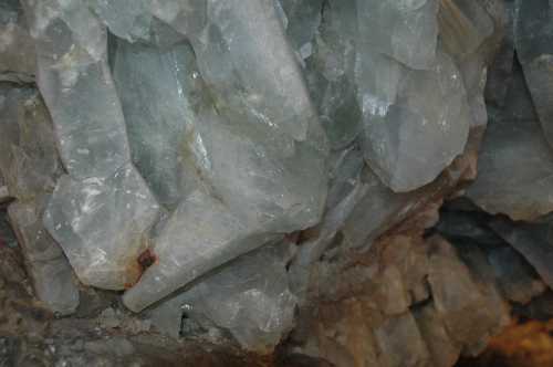 Close-up of translucent, light blue-green crystals with sharp edges, embedded in a rocky surface.